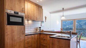 A modern kitchen with wooden cabinets, a built-in oven, a sink, and a window overlooking a balcony. - Holiday Apartment 'Thusnelda A' with Mountain View, Balcony & Wi-Fi (Seis am Schlern)