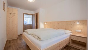 Un dormitorio con cama de madera, mesita de noche, armario de madera y una puerta que da a otra habitación.
