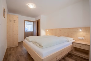 A bedroom with a wooden bed, a nightstand, a wooden wardrobe, and a door leading to another room. - Apartment 'Thusnelda B' with Mountain View, Balcony & Wi-Fi (Seis am Schlern)