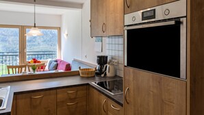 Una cocina con armarios de madera, horno de acero inoxidable y ventana con vista a un balcón.