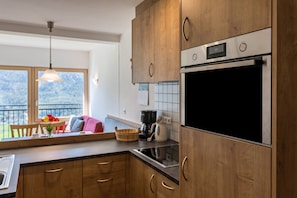 A kitchen with wooden cabinets, a stainless steel oven, and a window overlooking a balcony. - Apartment 'Thusnelda B' with Mountain View, Balcony & Wi-Fi (Seis am Schlern)