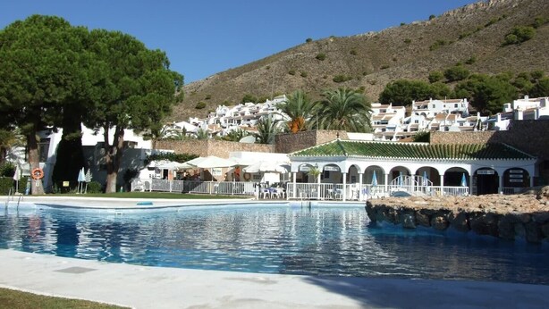 A swimming pool with a white fence, a bar area, and a view of white buildings on a hillside.