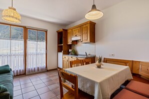 Cozinha com armários de madeira, mesa de jantar com toalha e porta de vidro deslizante para uma varanda.