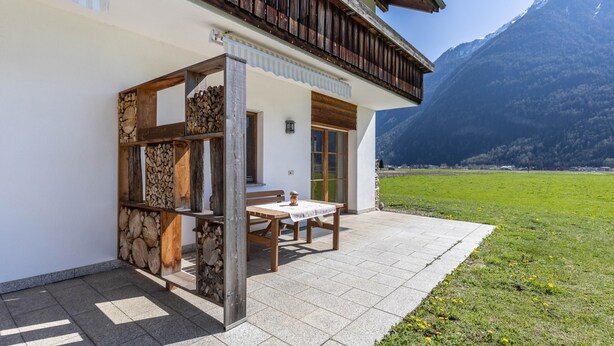 Eine Chalet mit Holzterrasse, Steinmauer und Bergblick.