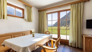 Ein Essbereich mit Tisch, Stühlen, einem Fenster mit Vorhängen und Blick auf Berge.