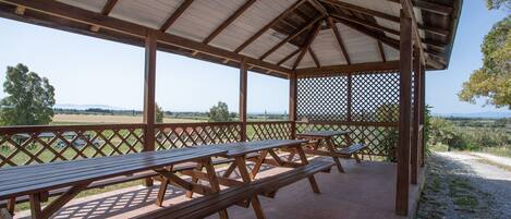 A covered picnic area with wooden benches and a lattice fence, overlooking a rural landscape.