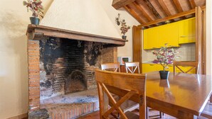 A rustic interior with a brick fireplace, wooden dining table, and yellow cabinets. - Cerboli Apartment with Sea View, Wi-Fi, Pool, and Air Conditioning (Riotorto)