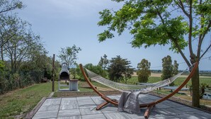 A hammock on a tiled patio with a view of a vineyard and trees.
