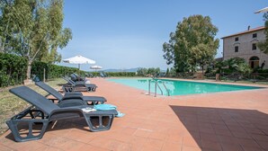 A pool area with lounge chairs and umbrellas, a swimming pool, and a building with a tiled roof.