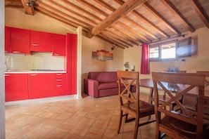 A kitchen with red cabinets, a wooden dining table, and a red sofa in a room with a sloped ceiling.