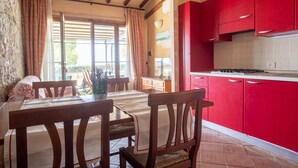 Ein Essbereich mit Tisch und Stühlen, eine Küche mit roten Schränken und ein Fenster mit Vorhängen.