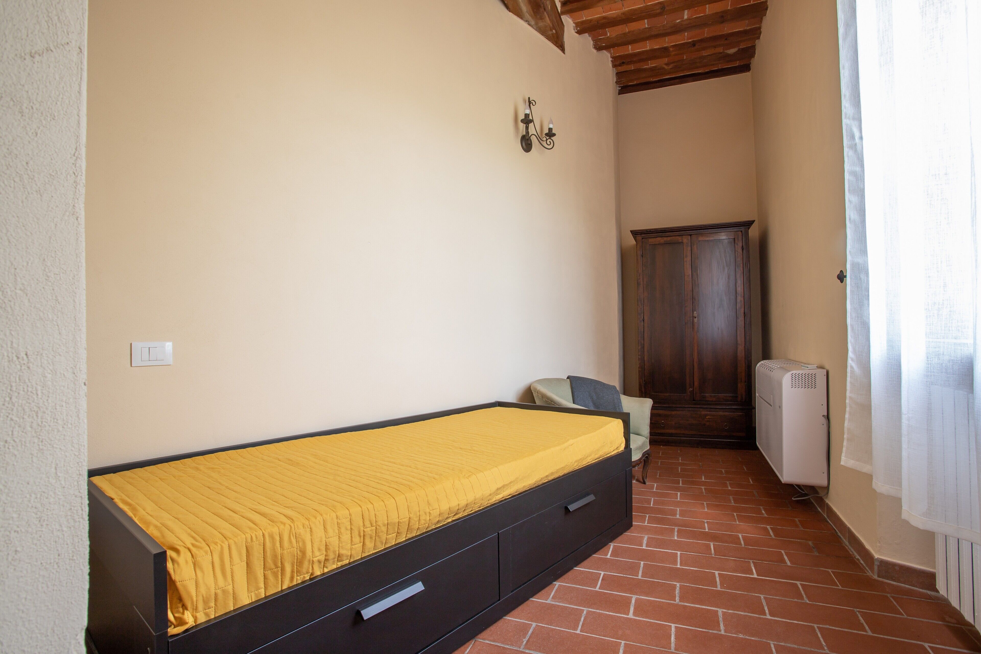 Ein Zimmer mit Bett, Stuhl, Kleiderschrank und Heizkörper.