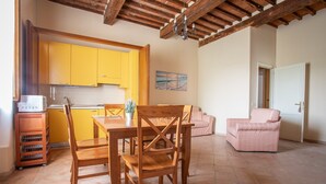 A kitchen with yellow cabinets, a dining table with chairs, a pink armchair, and a tiled floor. - Apartment "Giannutri" with Sea View, Wi-Fi, Pool & A/C (Riotorto)