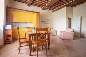 A kitchen with yellow cabinets, a dining table with chairs, a pink armchair, and a tiled floor.