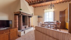 A living room with a brick fireplace, wooden furniture, a TV, and a dining area with a table and chairs. - Apartment "Giannutri" with Sea View, Wi-Fi, Pool & A/C (Riotorto)