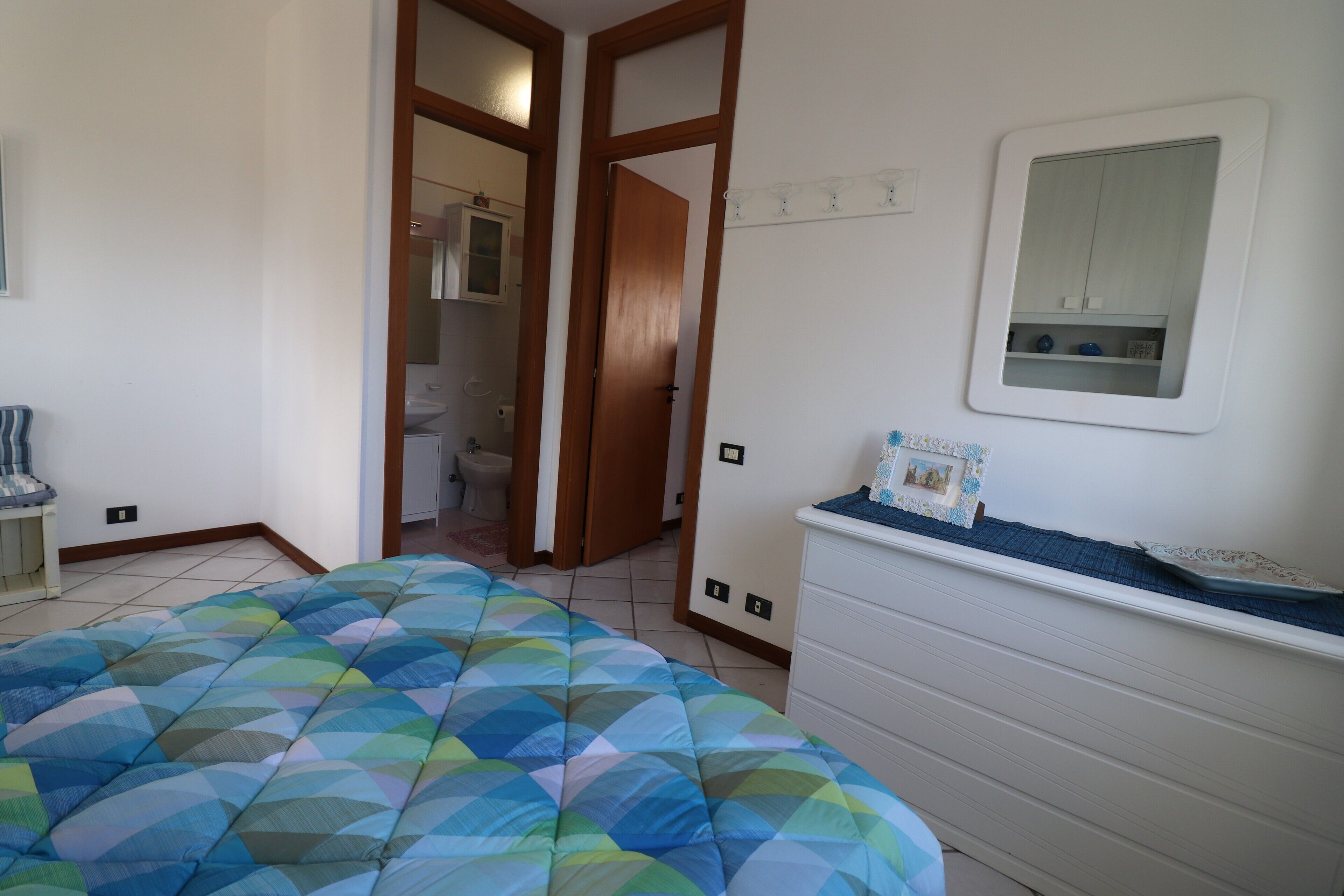 A bedroom with a bed, a dresser, a mirror, and a door leading to a bathroom.