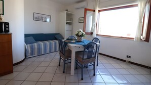 A room with a dining table, chairs, a sofa, a cabinet, and a window with curtains.