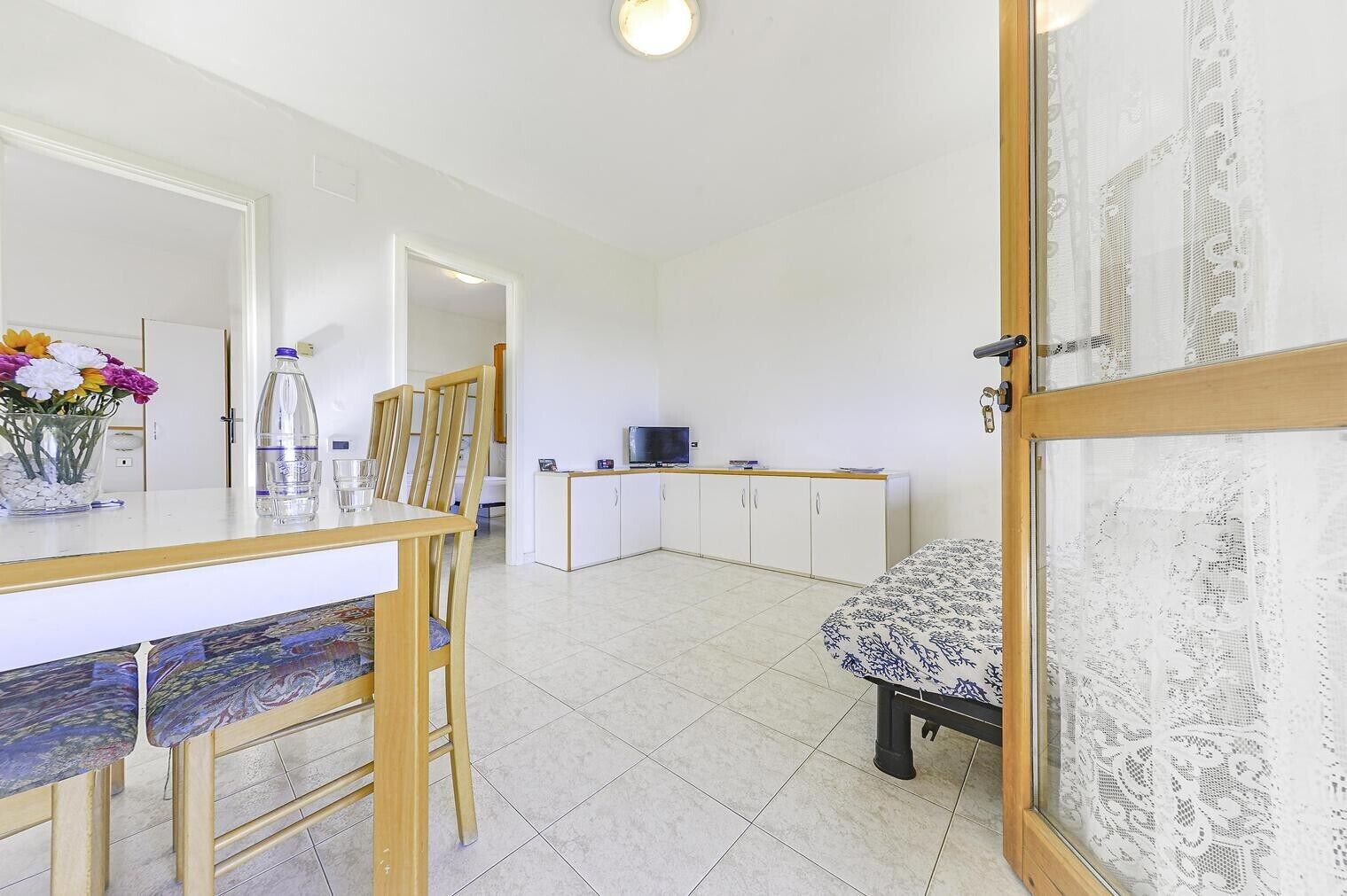 Una stanza con un tavolo da pranzo, sedie, un letto con copriletto decorato, una televisione e un armadio.