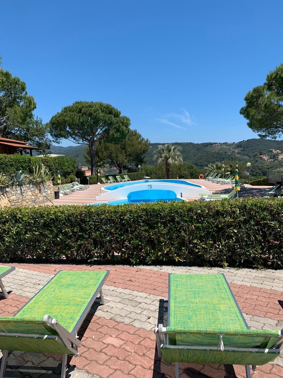 A pool area with lounge chairs, a clear blue sky, and a view of hills.