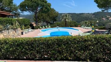 A pool area with lounge chairs, a clear blue sky, and a view of hills.