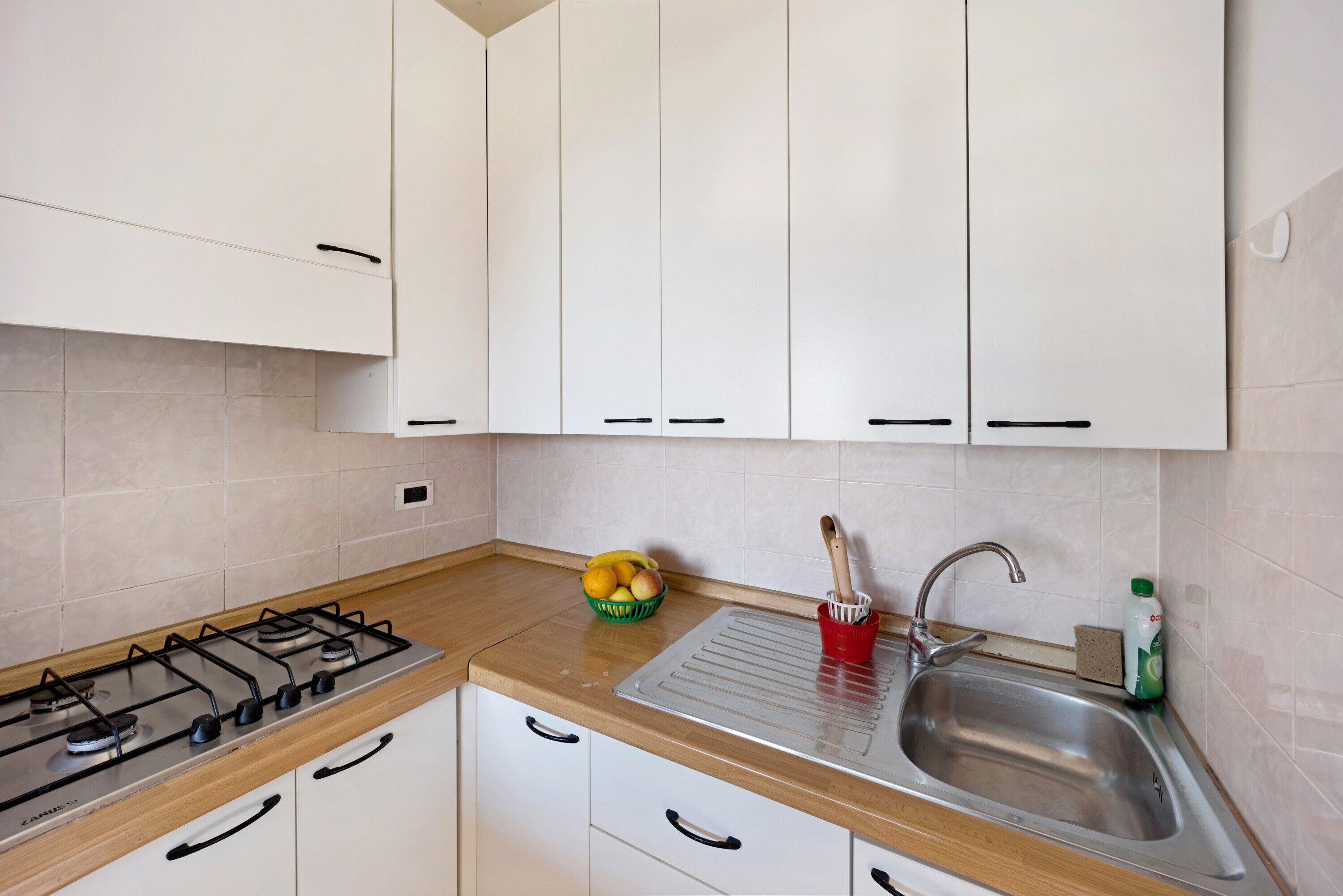 A kitchen with white cabinets, a gas stove, a sink, and a fruit bowl on the countertop.