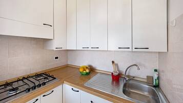 A kitchen with white cabinets, a gas stove, a sink, and a fruit bowl on the countertop.