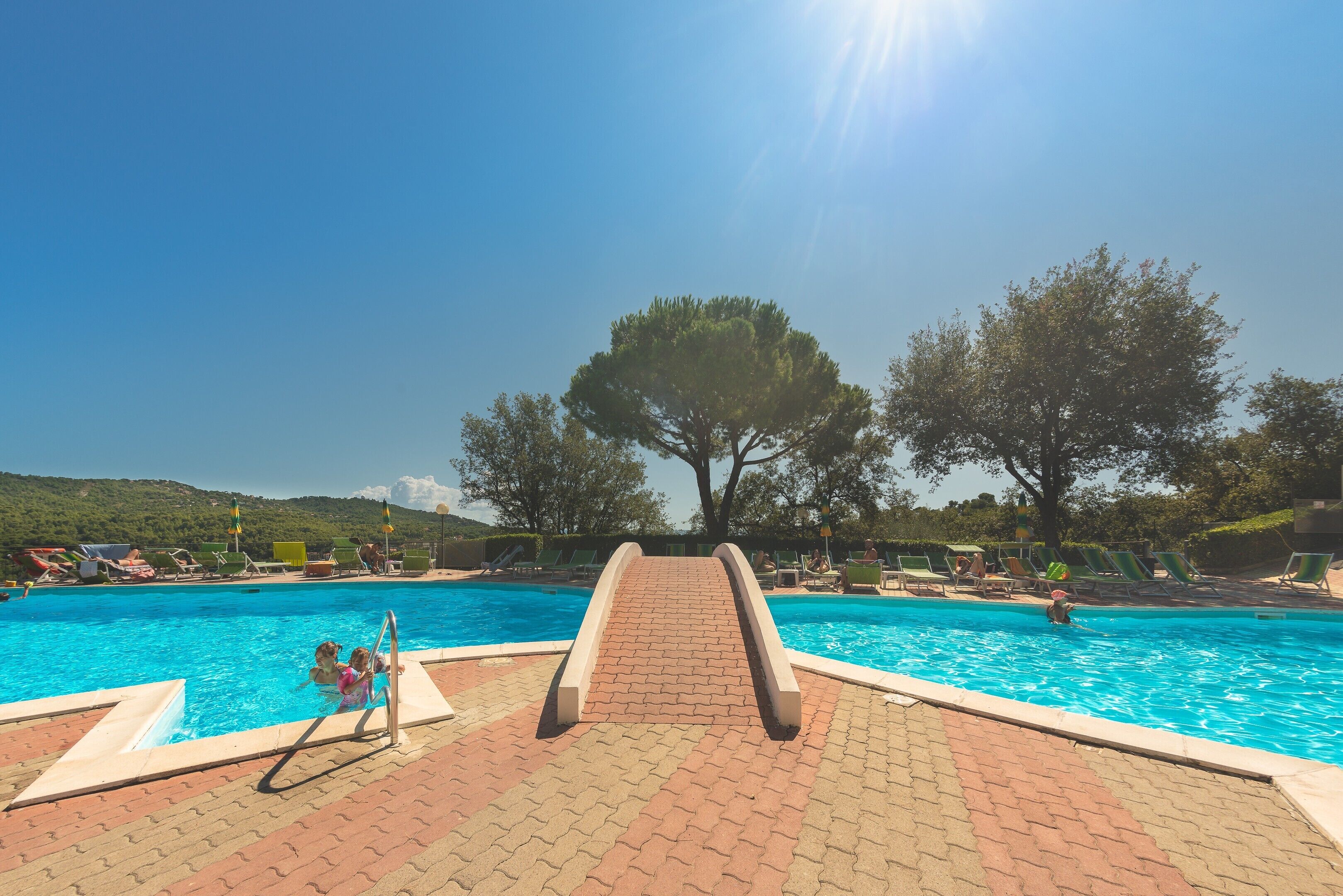 Une piscine avec un toboggan, des chaises longues et des arbres en arrière-plan.