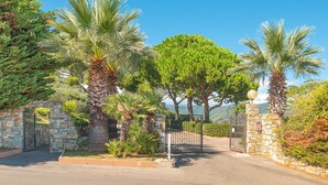A gated entrance with stone walls, palm trees, and a clear sky. - New Management Holiday Home Villaggio Colombo V3 with Garden & Shared Pool (Andora (SV))