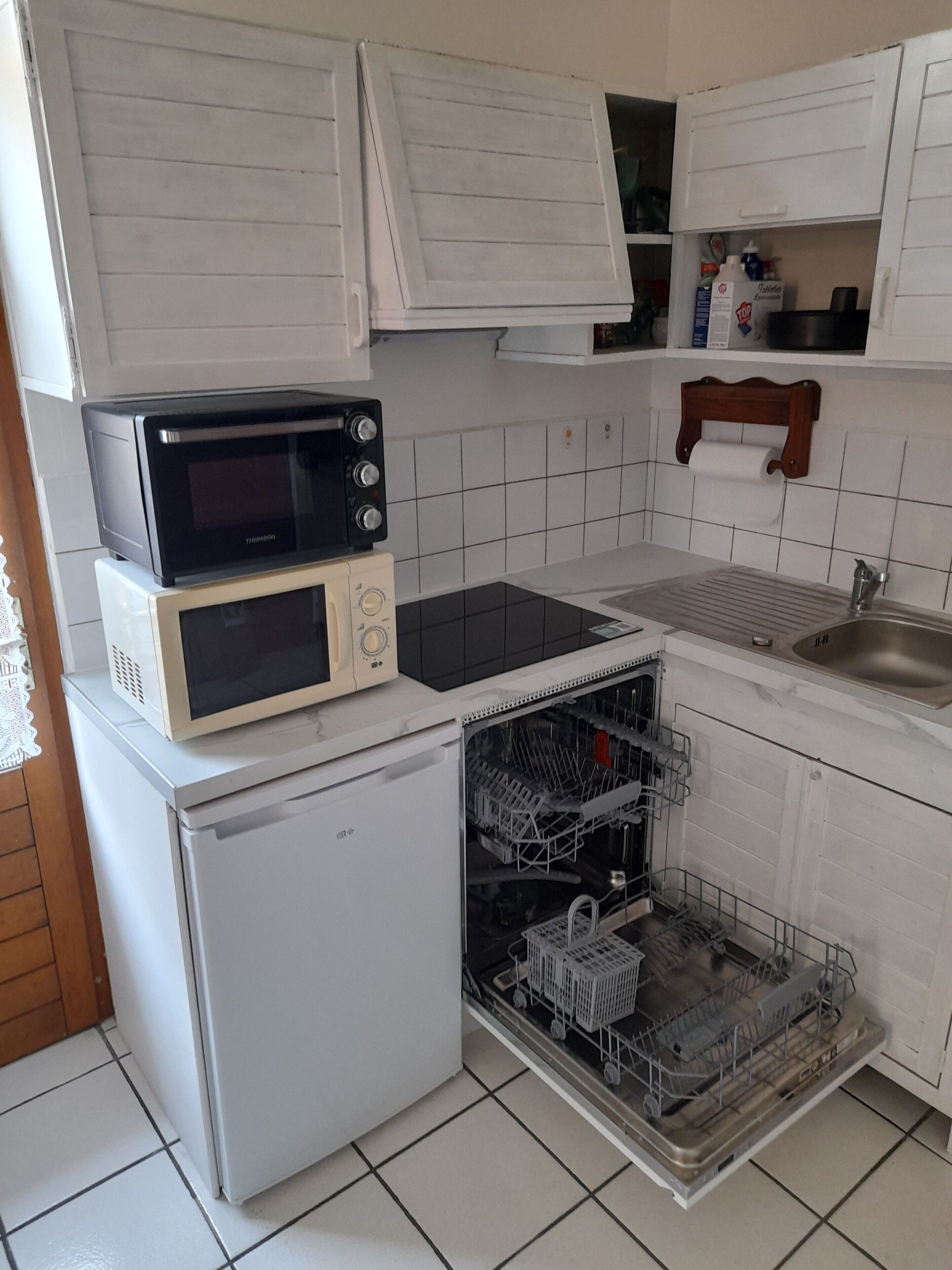 Eine kompakte Küche mit Mikrowelle, kleinem Kühlschrank und Geschirrspüler.