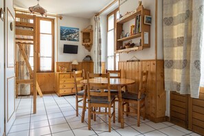 Un intérieur en bois comprenant une table à manger, des chaises, un téléviseur, une bibliothèque et une fenêtre donnant sur la montagne.