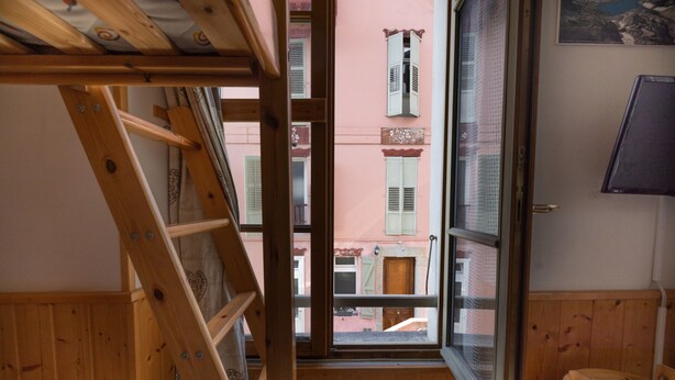 Een kamer met een houten ladder, een raam met uitzicht op gebouwen en een houten deur.