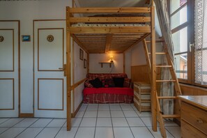 Une chambre avec un lit superposé, une échelle en bois, un canapé rouge et une petite table.