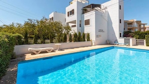 Una piscina con sillas de descanso, un edificio blanco con la señalización 'vista mobile' y follaje.