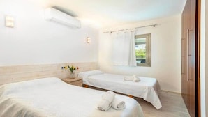 Habitación de hotel con dos camas, una ventana con cortinas, un equipo de aire acondicionado y una mesita de noche con un florero.