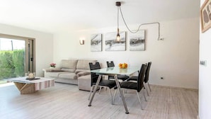 Una sala moderna con una mesa de comedor de vidrio, sillas negras, un sofá beige y arte abstracto en la pared.