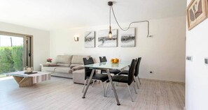 Un salon moderne avec une table à manger en verre, des chaises noires, un canapé beige et des œuvres d’art abstraites accrochées au mur.