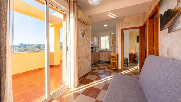 Een ruime woonkamer met een zwart-wit betegelde vloer, een bank, een balkon met uitzicht en een keuken op de achtergrond.