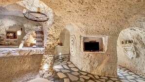 Un intérieur aux murs de pierre, avec une cheminée et un sol recouvert de carreaux de pierre.
