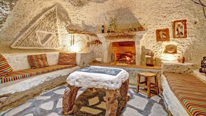 Un intérieur chaleureux avec une cheminée en pierre, un tabouret en bois et un banc agrémenté de coussins à rayures.