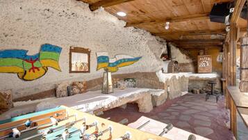 A rustic interior with a foosball table, stone walls, and a wooden ceiling.