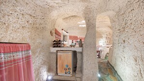 Une pièce aux murs de pierre, avec un meuble en bois, une nappe à carreaux rouges et blancs, et un sol carrelé.