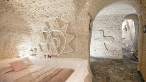 Une pièce aux murs de pierre, avec un lit, un sol en pierre et une porte donnant sur une autre pièce.