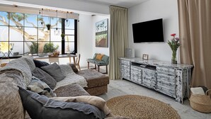 Una sala de estar con un sofá, una mesa de centro, un televisor y un ventanal con cortinas.