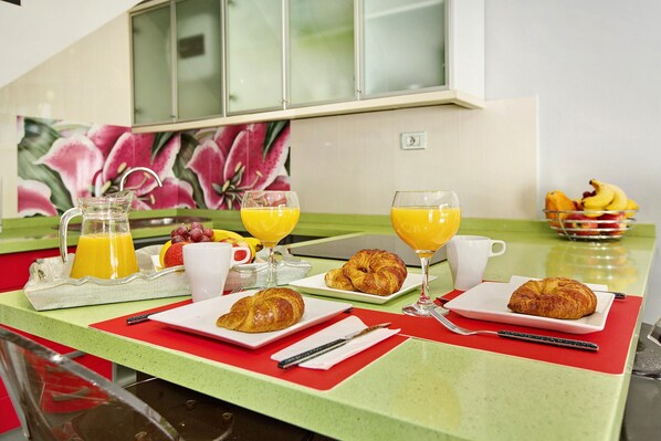 Un plateau de petit-déjeuner avec des croissants, du jus d’orange et un saladier de fruits, posé sur un comptoir de cuisine.