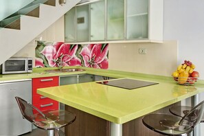 Une cuisine avec un plan de travail vert, des tiroirs rouges, un four à micro-ondes, un évier et un panier à fruits.