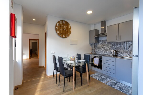 A modern kitchen with a dining table, chairs, a clock, and a patterned backsplash.