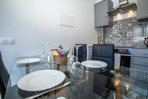 A modern kitchen with a tiled backsplash, a dining table set with plates, glasses, and cutlery, and a seating area with chairs.