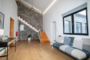 A modern living room with a wooden staircase, a sofa with cushions, a dining table, and a potted plant.
