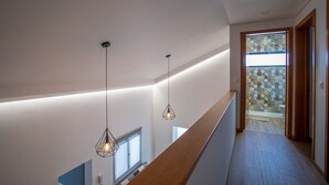 Ein modernes Interieur mit einer Holztreppe, Pendelleuchten und Blick in ein Badezimmer mit gemusterten Fliesen.
