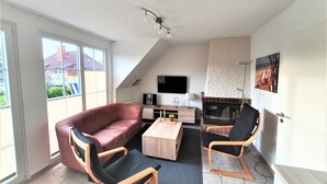 Ein modernes Wohnzimmer mit einer Couch, zwei Sesseln, einem Couchtisch, einem Kamin und einem Fernseher.